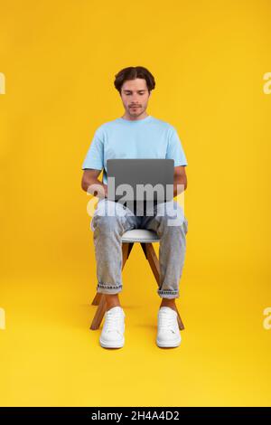 Portrait of serious bearded guy sitting on chair using laptop computer, reading news, watching video or movie, working or elearning remotely, isolated Stock Photo