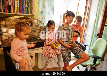 Four children holding their favorite pets on hands. Kids playing with hamster,turtle and parrots at home. Stock Photo