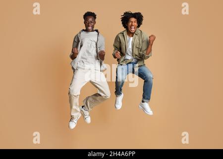 Big Joy. Two Happy Excited Black Guys Jumping In Air And Celebrating Success, Overjoyed Millennial African American Friends Emotionally Reacting To Wi Stock Photo