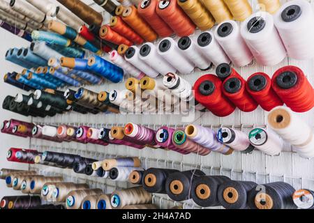 Many thread spool, cotton yarn roll, sewing material on wall in dressmaking studio, fabric. Colorful embroidery thread spool in sewing studio Stock Photo