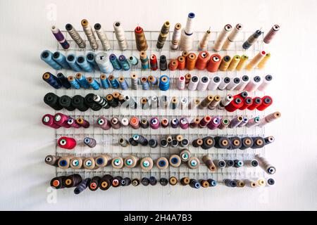 Many thread spool, cotton yarn roll, sewing material on wall in dressmaking studio, fabric. Colorful embroidery thread spool in sewing studio Stock Photo