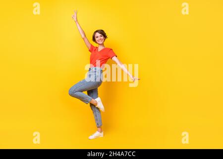 Full size profile photo of cool brunette optimistic lady dance wear red t-shirt jeans sneakers isolated on yellow color background Stock Photo