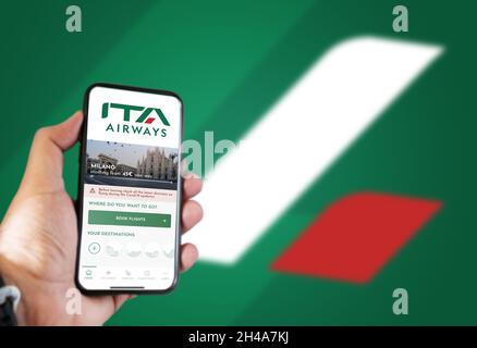 Rome, IT, October 2021: hand holding a phone with the ITA Airways app on the screen and the logo blurred on a green background.ITA Airways is the new Stock Photo