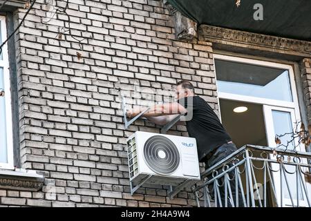 Dnepropetrovsk, Ukraine - 10.22.2021: A worker installs the bracket for the outdoor unit of the air conditioner on the wall of the house. Stock Photo