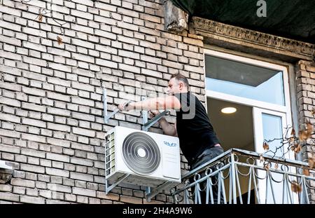 Dnepropetrovsk, Ukraine - 10.22.2021: A worker installs the bracket for the outdoor unit of the air conditioner on the wall of the house. Stock Photo