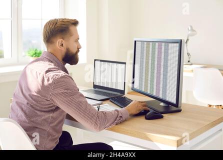 Accountant sitting at his office desk and working with data on multiple computers Stock Photo
