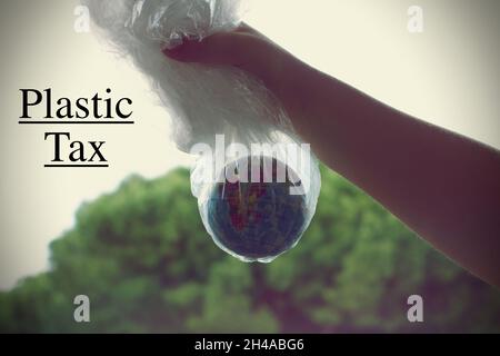 Hand of a boy holding a Globe inside a plastic bag with the text "Plastic tax" Stock Photo