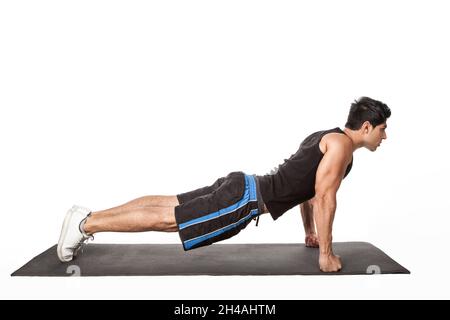 Portrait of strong handsome athletic man standing in plank position, working out on fitness mat, doing Phalakasana exercise on straight arms. Indoor studio shot isolated on white background. Stock Photo