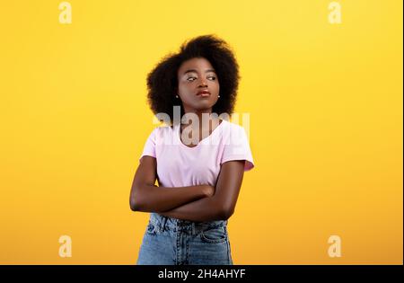 Portrait of serious african american lady looking aside and posing with folded arms over yellow studio background. Confident black woman crossing hand Stock Photo