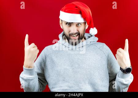 a bearded man in a red Santa Claus hat grins and makes various poses with his hands. Stock Photo