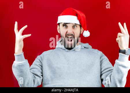 a man in a red Santa Claus hat makes different poses and gestures with his hands and yells. Stock Photo