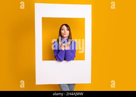 Photo of flirty cute young woman wear purple pullover holding big white paper photo frame isolated yellow color background Stock Photo