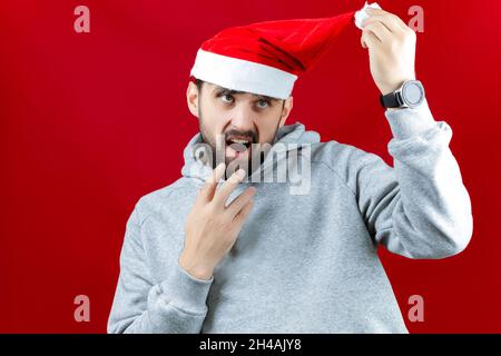 a man in a red Santa Claus hat makes different poses and gestures with his hands and yells. Stock Photo