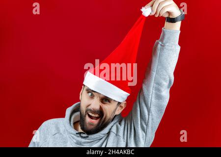 a cheerful bearded man in a red Santa Claus hat pulls the bubo of this hat to the side. Stock Photo