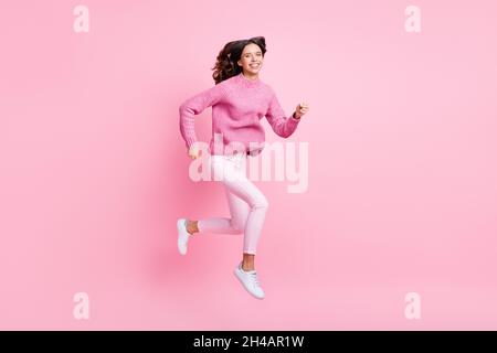 Full size profile photo of optimistic cool brunette lady jump run wear pink sweater trousers sneakers isolated on pink color background Stock Photo