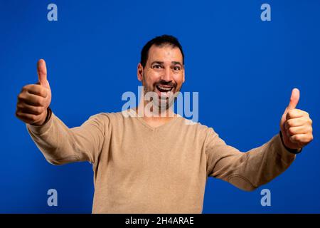 Young handsome man approving doing positive gesture with hand, thumbs up smiling and happy for success. winner gesture. Stock Photo