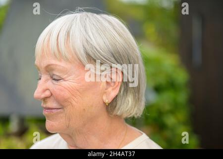 Smiling senior woman with serene expression and closed eyes in a close up headshot portrait outdoors in a garden Stock Photo