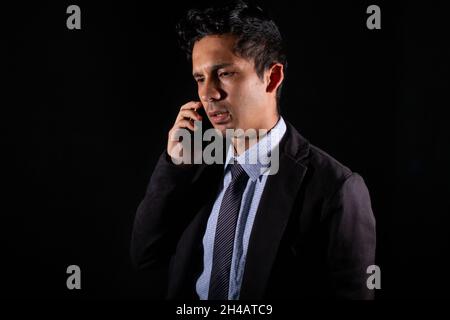 Young adult businessman talking on the phone. Business man, serious and worried making a call, isolated on black background. Stock Photo