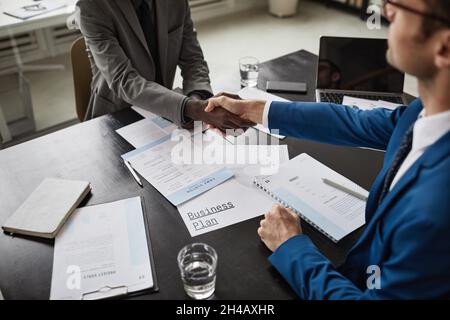 Close up of two businessmen shaking hands over table during meeting in office, copy space Stock Photo