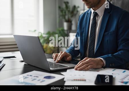 Cropped shot of successful businessman in suit working at able in office and using laptop, copy space Stock Photo