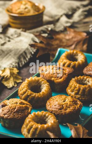 Homemade delicious mini bundt cakes, guglhupf, muffins on a blue plate on rustic wooden background with autumn decoration, vertical Stock Photo
