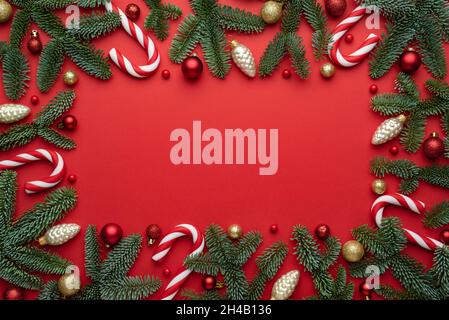 Red Christmas background with decorative frame made of fir branches and tree decorations. Flat lay, top view and copy space for text Stock Photo