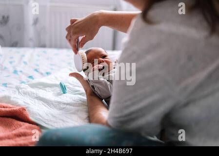 Mother combing her baby's hair in bed. Stock Photo