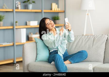 Beautiful young Indian woman using mobile phone, checking messages, searching internet or watching movie at home. Happy Eastern lady chatting to frien Stock Photo