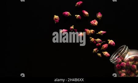 Dry roses' heads scattered from a glass jar on a black background Stock Photo