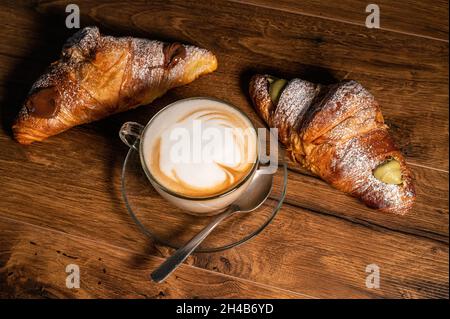 sweet croissants with cream and cappuccino on a wooden surface Stock Photo