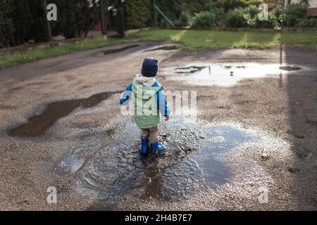 Toddler boy in green and blue jacket and blue wellingtons walkin Stock Photo