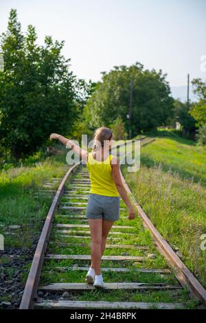 a woman in a yellow jersey walks along the train tracks Stock Photo