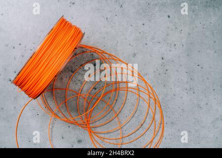 3d Printer Plastic Filament. Spool of orange  thermoplastic wire for 3D printing close up on grey stone background, flat lay Stock Photo