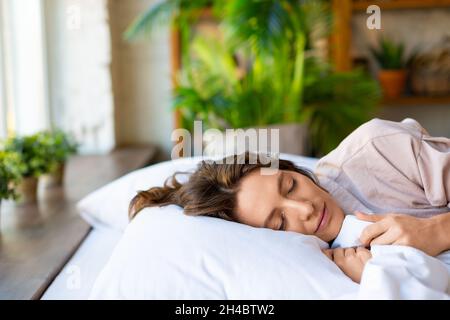 Close up view: a young woman is sleeping embracing a blanket. The concept of recuperation and healthy sleep. Stock Photo