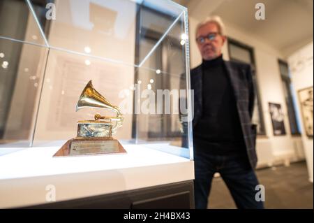 11 October 2021, Lower Saxony, Lüneburg: Carsten Junge, director of the Kunsthalle der Sparkassenstiftung Lüneburg, is standing next to a golden Grammy, which Klaus Voormann received for the Best Album Cover. Klaus Voormann is considered the fifth Beatle, he met the Beatles in 1960 in the Kaiserkeller on St. Pauli. In the Kultur Bäckerei Lüneburg an exhibition is dedicated to his life's work for the first time. (to dpa 'Klaus Voormann - no one was as close to the Beatles') Photo: Philipp Schulze/dpa Stock Photo