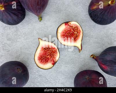 Flat-lay of purple figs, whole and halves on grey concrete. Top view and space for text. Stock Photo