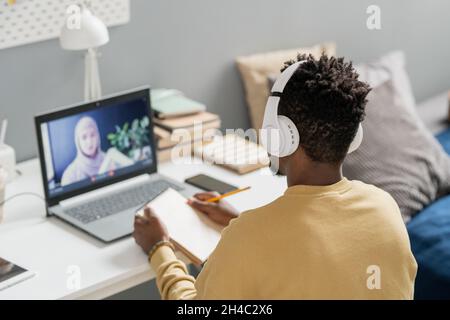 Young African male student in headphones looking at teacher on laptop screen explaining new subject during online lesson Stock Photo