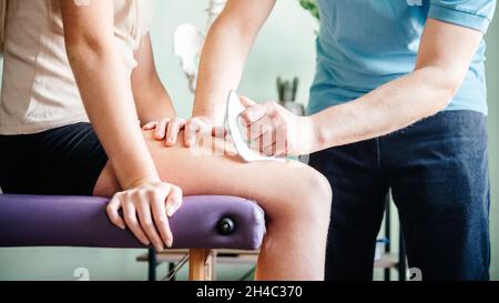 Therapist using IASTM instrument treatment, girl receiving soft tissue treatment on her leg with guasha stainless steel tool Stock Photo