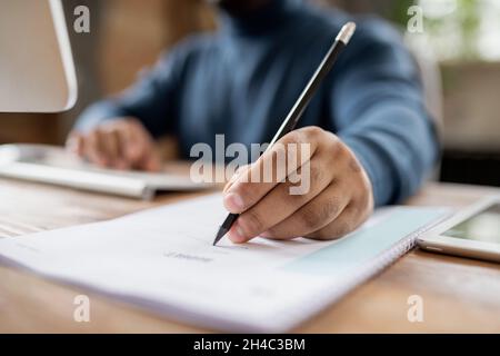 Hand of man holding pencil over document while sitting in front of computer and making notes during online lesson Stock Photo