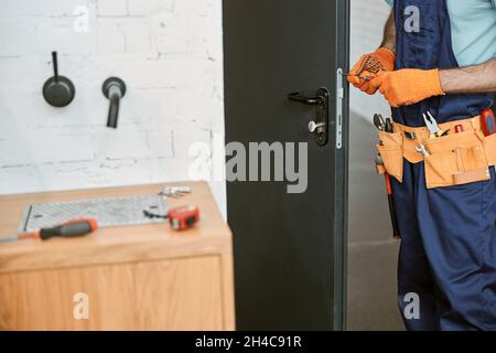 Male worker in gloves repairing door in building Stock Photo