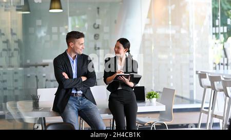 Happy diverse colleague partners leaning on the desk and talking about new campaign in the office. Stock Photo