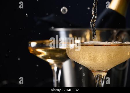 Pouring champagne to wine glasses on black background. 2022 New Year party. Close up. Festive holiday and celebration. Stock Photo