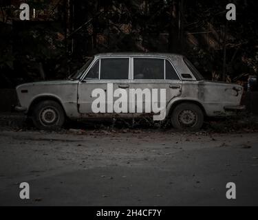 VRAT, BULGARIA - Apr 14, 2019: A grayscale shot of an abandoned white eastern-european car with rust along the side Stock Photo