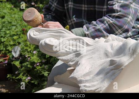 A Craftsman Using a Chisel to Carve a Stone Head. Stock Photo