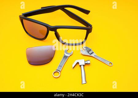 Broken plastic sunglasses with a set of work tools on a yellow background. Repairing accessories at home. Stock Photo