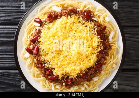 Homemade Cincinnati Chili Spaghetti with Red beans Cheese and Onion close up in the plate on the black wooden background. Horizontal top view from abo Stock Photo