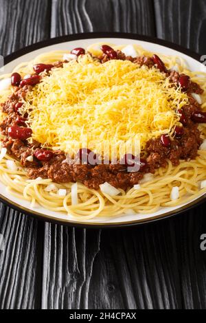 Authentic Cincinnati Chili is a meaty, rich, and uniquely spiced chili served over hot spaghetti with cheese toppings closeup in the plate on the blac Stock Photo