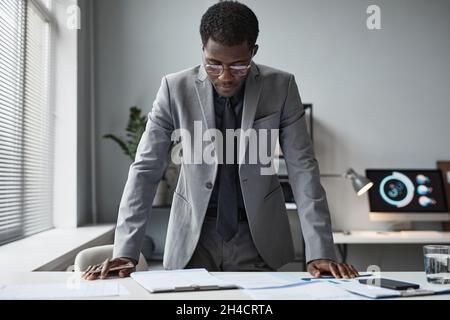 Portrait of successful black businessman leaning over desk in office and reading document, copy space Stock Photo