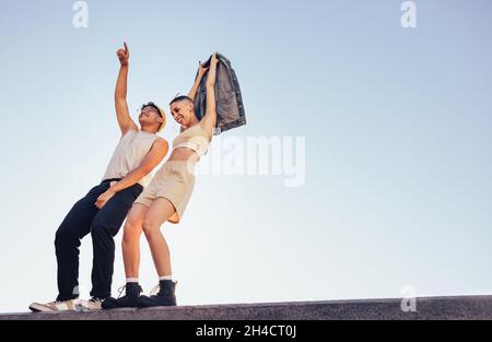 Hipsters dancing and having fun outdoors. Two energetic youngsters standing on a wall with the sky in the background. Two happy young friends feeling Stock Photo