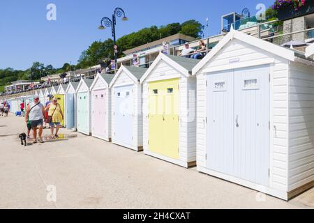 People walking past the pastel coloured Beach huts Lyme Regis beach Dorset Jurassic coast heritage coast England UK GB Europe Stock Photo